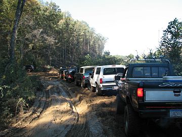 1989 Ford Bronco - Several vehicles are navigating a challenging muddy path in a wooded area.