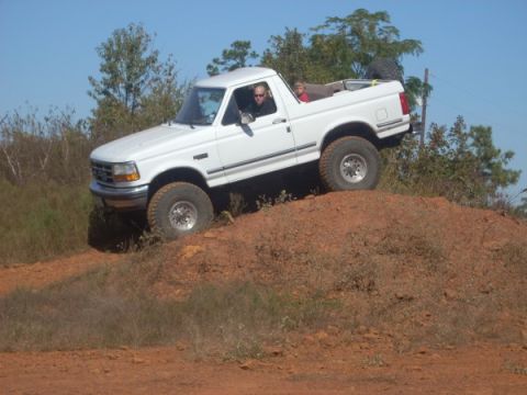 1992 Ford Bronco - White 1992 Ford Bronco navigates an off-road trail, ascending a steep dirt incline.