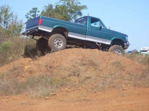 1992 Ford Bronco - A green pickup truck navigates a steep dirt incline under a clear blue sky.