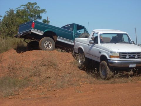 1992 Ford Bronco - Two Ford trucks, a white Bronco and a green F-150, navigate a challenging dirt terrain.