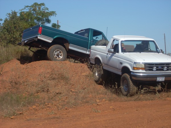 White 1992 Ford Bronco and green Ford F-150 off-roading on a dirt hill