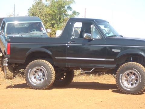 1992 Ford Bronco - A black 1992 Ford Bronco is seen from the side, with another vehicle partially visible behind it.