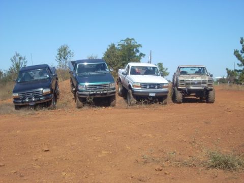 1992 Ford Bronco - Four pickup trucks are parked on a dirt incline under a clear blue sky.