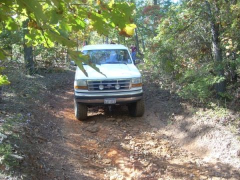 1992 Ford Bronco - A 1992 Ford Bronco navigates a wooded trail, with another vehicle visible in the background.