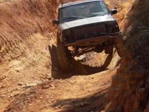 1992 Ford Bronco - Modified off-road vehicle tackling a challenging dirt trail with steep sides.