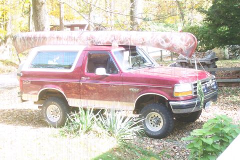 1993 Ford Bronco - A red 1993 Ford Bronco is parked outdoors with a camouflage canoe strapped to its roof.