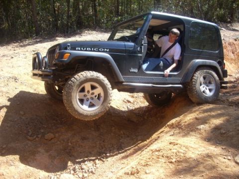 1992 Ford Bronco - Jeep Wrangler Rubicon tackles an off-road obstacle on a dirt trail.