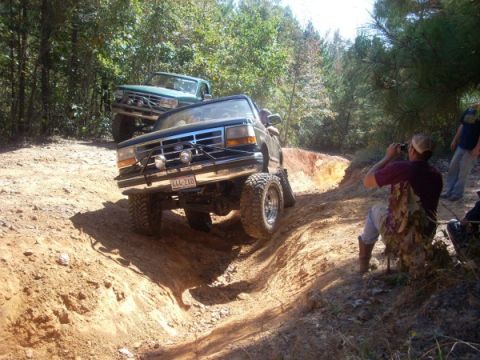1992 Ford Bronco - Two Ford Broncos navigate a challenging off-road course with onlookers.