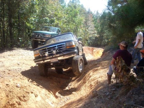 1992 Ford Bronco - Two trucks tackle a challenging off-road course on a sunny day.
