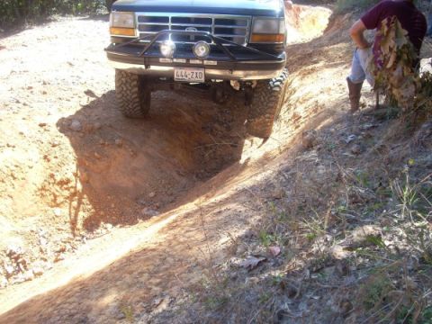1992 Ford Bronco - A person watches as a lifted Ford truck navigates a steep dirt path.