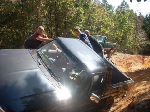 1992 Ford Bronco - A 1992 Ford Bronco is stuck in a ditch while several people attempt to push it out, with another truck visible in the background.