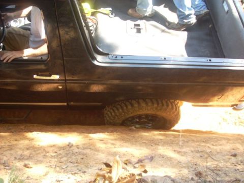 1992 Ford Bronco - A black SUV with aggressive tires is stuck in the dirt, showing its side profile and interior.