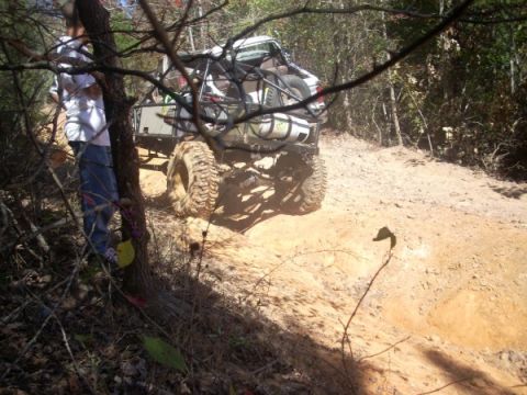 1992 Ford Bronco - A heavily modified off-road vehicle navigates a steep dirt path through a wooded area.