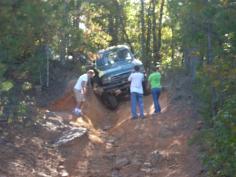 1992 Ford Bronco - People watch an off-road vehicle climb a challenging dirt trail in a wooded area.
