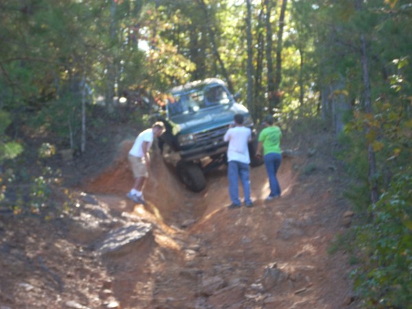 Off-road vehicle navigating a steep dirt trail with three people watching