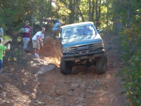 1992 Ford Bronco - A group of friends watch as a modified SUV navigates a challenging off-road obstacle on a sunny day.