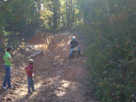 1992 Ford Bronco - A dirt bike rider navigates a challenging off-road trail with spectators.