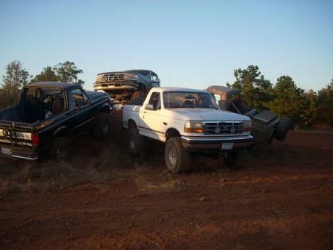 1992 Ford Bronco - Several trucks and SUVs are parked on a dirt hill under a clear sky.