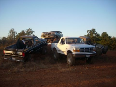 1992 Ford Bronco - A white 1992 Ford Bronco is seen off-roading with several other trucks and SUVs under a clear blue sky.
