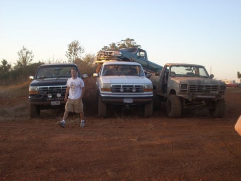 1992 Ford Bronco - A group of trucks are parked on a dirt lot, with a man posing in front of the first truck.
