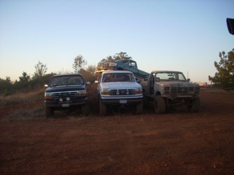 1992 Ford Bronco - Several lifted trucks are parked on a dirt hill under a clear sky.