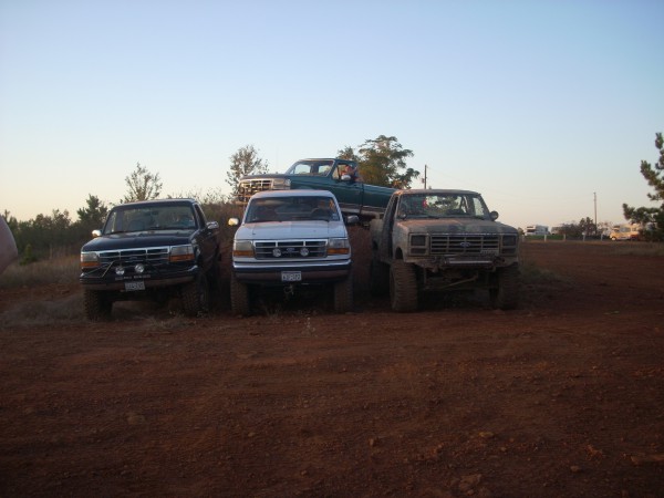 Three Ford trucks and one green pickup truck parked on a dirt hill