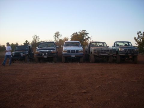 1992 Ford Bronco - A group of trucks and a Jeep are parked in a dirt lot under a clear sky.