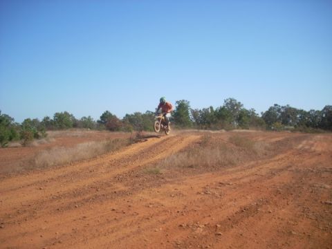 1992 Ford Bronco - A dirt bike rider catches air while navigating a rough track under a clear blue sky.