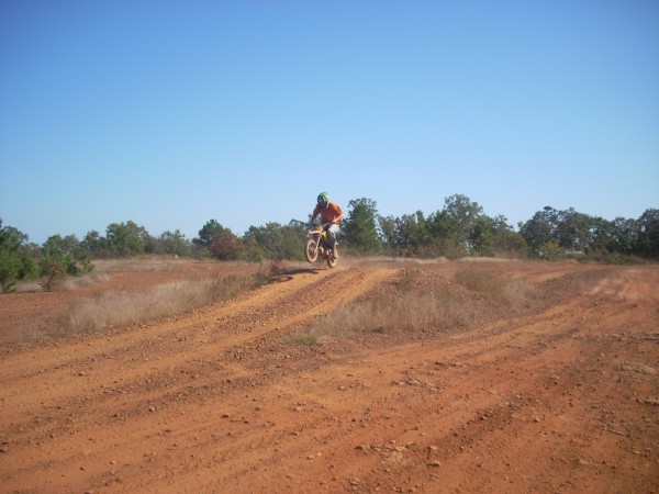 Dirt bike airborne over a dirt track, rider in orange shirt and helmet
