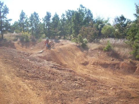 1992 Ford Bronco - A person on a dirt bike navigates a rough, sandy terrain with trees and brush visible in the distance.