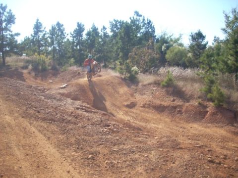 1992 Ford Bronco - A dirt bike rider is captured mid-air on a dusty hill with trees in the background.