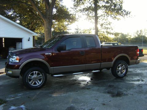 2005 Ford F-150 - This maroon and tan Ford F-150 pickup truck is seen from the side, parked on a wet concrete surface.