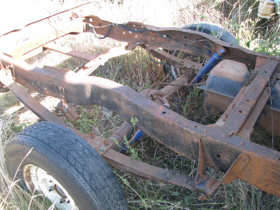 Rusty truck frame with leaf springs and a fuel tank, viewed from the side