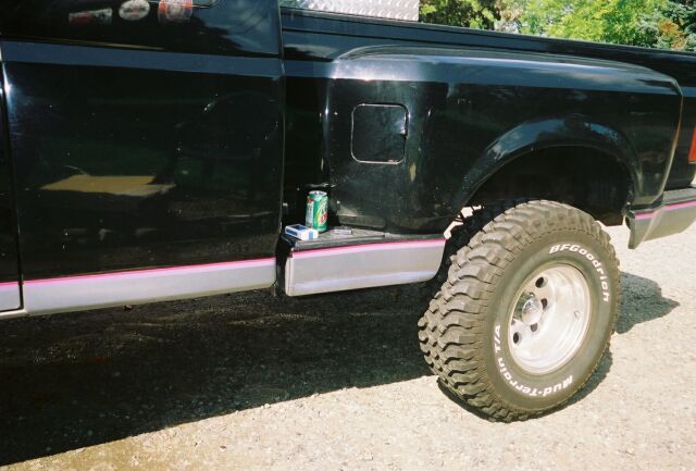 Side of a black lifted pickup with pink pinstripe, diamond-plate toolbox and BFGoodrich mud tire