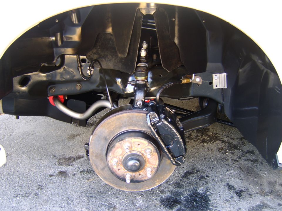 Front suspension and disc brake assembly with caliper and rotor under a vehicle fender