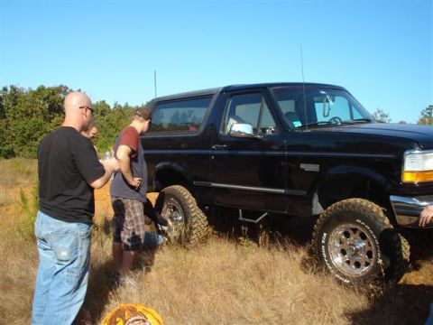 2008 International School Bus - A black SUV with off-road tires is parked on a grassy incline, with three men observing it.