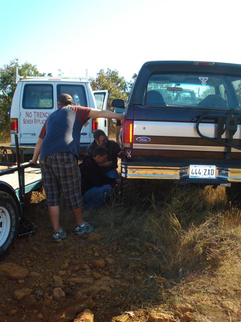 2008 International School Bus - A dark Ford Bronco is hitched to a trailer, with a white van visible behind it and people working near the hitch.