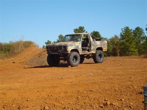 2008 International School Bus - Modified pickup truck with camouflage paint sits on a dirt lot under a clear blue sky.