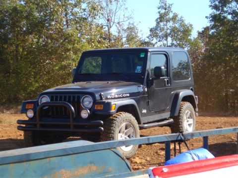 2008 International School Bus - A black Jeep Wrangler Rubicon is parked on a dirt path, with trees and a trailer visible.