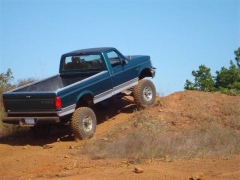 2008 International School Bus - A lifted green Ford F-150 navigates an off-road course under a clear blue sky.