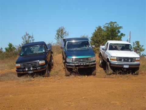 2008 International School Bus - Three Ford F-150 pickup trucks from the mid-1990s are parked on a dirt incline under a clear blue sky.