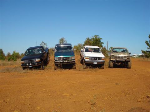 2008 International School Bus - Four pickup trucks are parked on a dirt incline with trees and a clear blue sky in the background.