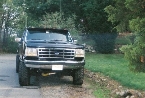 1994 Ford F-150 - A black 1994 Ford F-150 pickup truck is parked on a dirt road with trees in the background.