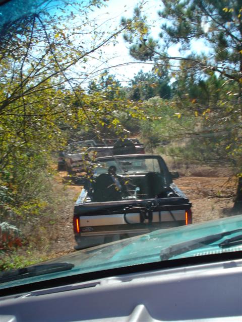 2008 International School Bus - A line of pickup trucks drives down a dirt road surrounded by trees.