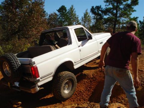2008 International School Bus - A white Ford Bronco navigates a dirt trail with a person standing nearby.