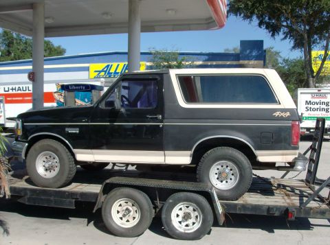 1992 Ford Bronco - A black 1992 Ford Bronco with beige trim and a 4x4 decal is loaded onto a trailer.