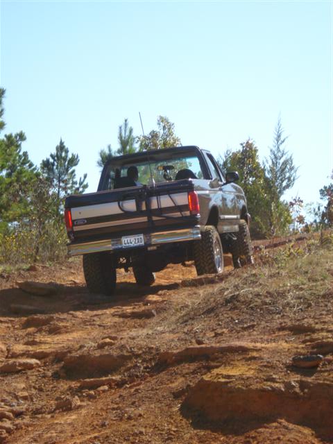 2008 International School Bus - A lifted brown pickup truck navigates a rough dirt path on a sunny day.