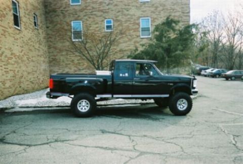 1994 Ford F-150 - A black pickup truck is parked on cracked pavement in front of a brick building.