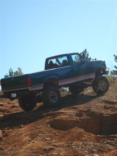 2008 International School Bus - A lifted pickup truck navigates a steep, rocky incline under a clear blue sky.