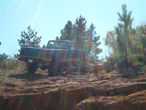 2008 International School Bus - A dark pickup truck is seen from the side, climbing a steep, rocky trail under a bright sky.